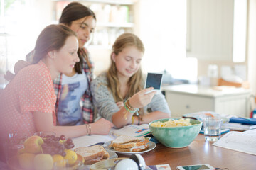 Three teenage girls looking at photograph while sitting at table