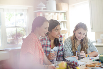 Teenage girls learning at table in kitchen
