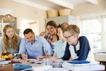 Teenagers with mid adult man sitting at table in dining room