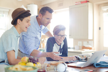 Teenage boys with father using laptop in dining room