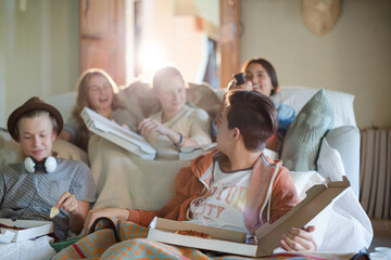 Group of teenagers eating pizza on sofa in living room