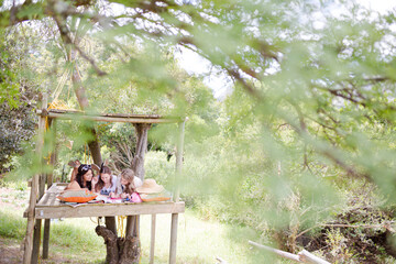 Three teenage girls reading magazine while lying in tree house in summer