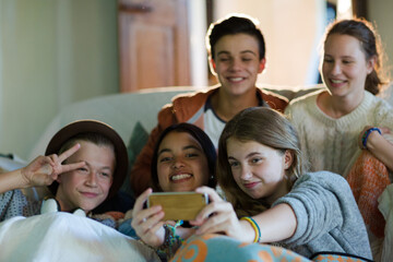 Group of teenagers taking selfie on sofa in living room