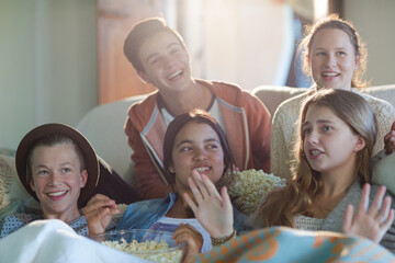 Group of teenagers having fun while watching tv on sofa