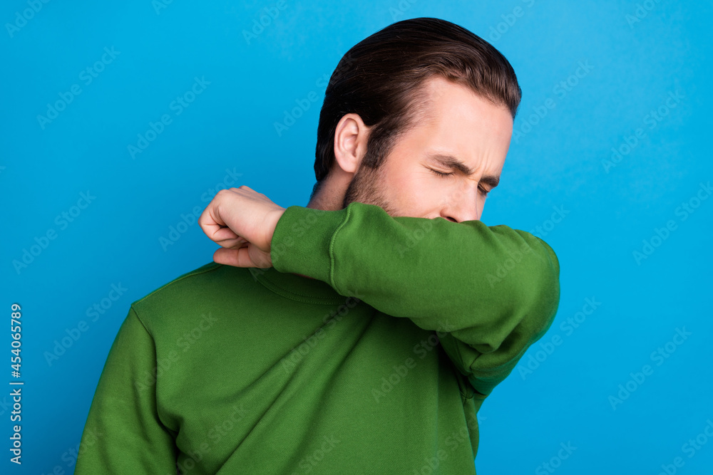 Sticker Photo of young unhappy unwell sick man coughing sneezing cover face hand covid-19 isolated on blue color background