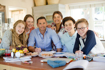 Group of teenagers with mid adult man sitting at table in dining room