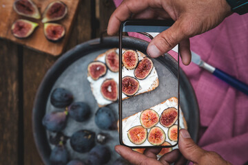 Man hands takes picture of food on the table with the phone. Breakfast. Sandwich with soft ricotta and figs. Smartphone photo for social media or blog post. Vegetarian, healthy, organic