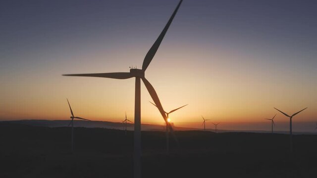 Wind generator rotate on mountain ridge close-up. Sunset soft light. Lilac and orange evening sky. Green energy. Clean natural source power. Future environment planet save. Slow motion aerial panorama