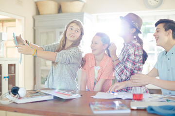 Group of smiling teenagers taking selfie in dining room