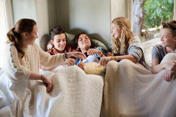 Group of teenagers throwing popcorn on themselves on sofa