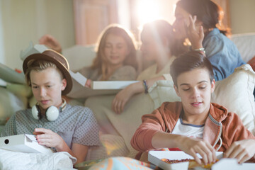 Group of teenagers eating pizza on sofa in living room