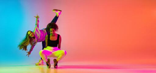 Emotive dance. Two beautiful stylish hip-hop girls dancing on colorful gradient background in neon...