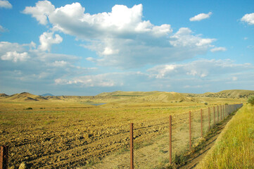 Fototapeta na wymiar A field fenced with a chain-link fence. Sandy mountains and a lake on the horizon. The road to Cape Meganom. Crimea.