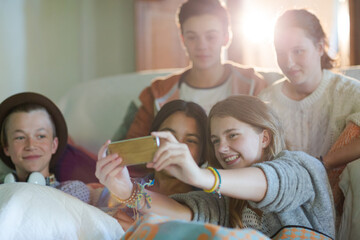 Group of teenagers taking selfie on sofa in living room