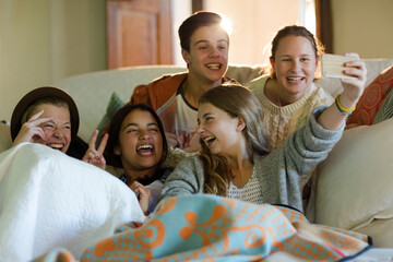 Group of teenagers taking selfie on sofa in living room