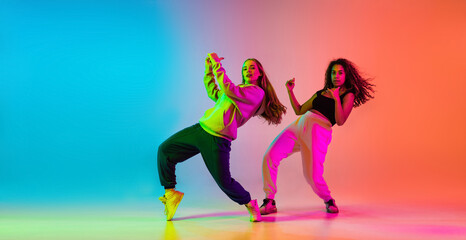 Two beautiful talented hip-hop dancers on colorful gradient background in neon lights
