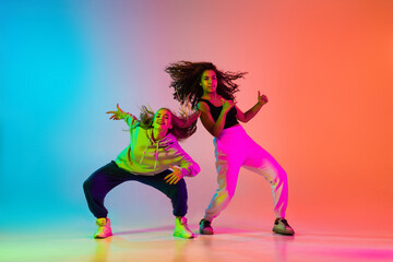 Two beautiful stylish hip-hop dancers on colorful gradient background in neon lights