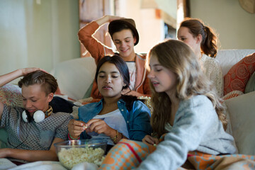 Group of teenagers throwing popcorn on themselves while sitting on sofa