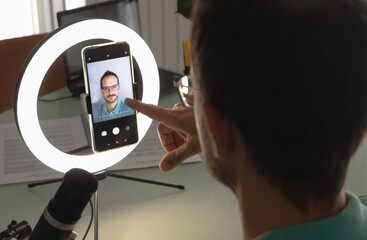 one man setting up a video call with his smart phone and a light ring studio lamp - Powered by Adobe