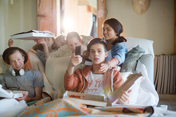 Group of teenagers eating pizza on sofa in living room