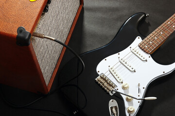 Naklejka premium Brown tube combo amplifier for electric guitar with black guitar on black background.