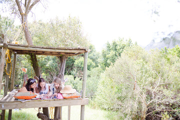 Three teenage girls reading magazine while lying in tree house in summer