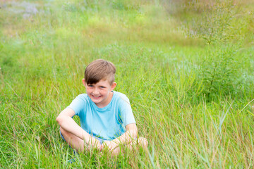 European child on the field, smiling little boy in a blue T-shirt on a background of grass