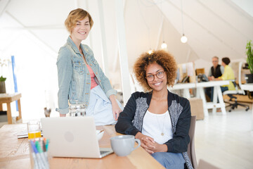 Portrait of women smiling in office with laptop on desk
