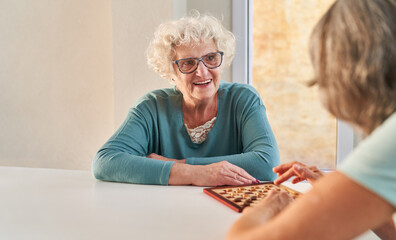 Happy elderly woman plays checkers with a friend
