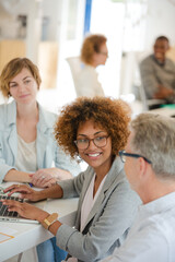 Three office workers talking at desk with laptop