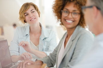 Three office workers talking at desk with laptop