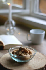 Bowl of cookies, cup of hot beverage, open book and lit candles on a table. Selective focus.