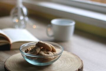 Bowl of cookies, cup of hot beverage, open book and lit candles on a table. Selective focus.