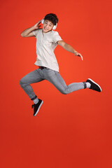 Fototapeta na wymiar Full-length portrait of young man jumping isolated over red studio background with copyspace for ad. Concept of human emotions, fashion, beauty, youth