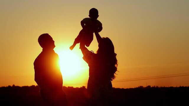 Unrecognizable silhouette of family at sunset, mom tosses the baby, family values and parental love