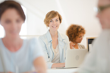Fototapeta premium Portrait woman sitting at desk, using laptop smiling in office, colleagues