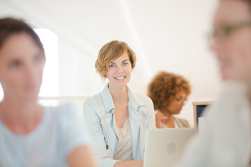 Fototapeta premium Portrait woman sitting at desk, using laptop smiling in office, colleagues