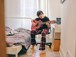 Teenage boy playing acoustic guitar in bedroom