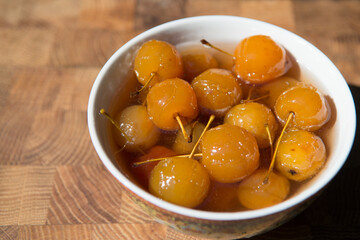 Jam made from whole apples of yellow ranetki in a porcelain cup on a wooden countertop.