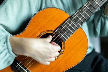Woman strumming strings of wooden solid acoustic guitar.