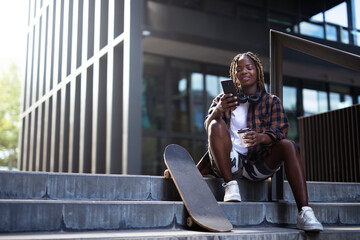 Beautiful african-american woman with skateboard. Young stylish woman with skateboard using the phone outdoors