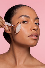 Studio portrait of beautiful woman doing face massage with rose quartz roller