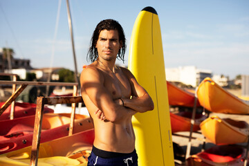 Portrait of handsome surfer with his surfboard. Young man with a surfboard on the beach.