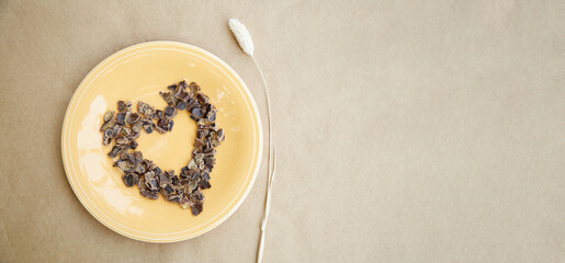 Carob - plant-based alternative - natural product on the plate with dry Lagurus ovatus grass a in shape of heart. Extra wide banner. Organic antioxidants and protein. Top view.