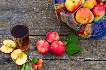 Seasonal harvest concept, ripe garden apples in a basket on a wooden table, freshly squeezed apple juice in a glass, rustic style