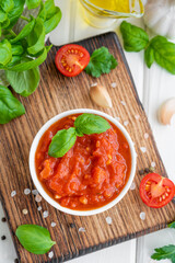 Traditional Italian marinara sauce in a bowl on a white wooden background with spices and ingredients. Top view. Copy space.