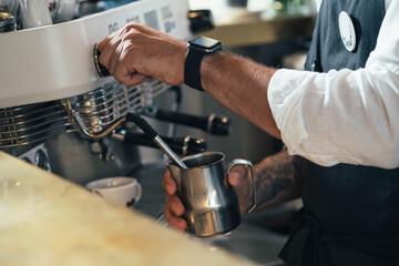 An Anonymous Barista Making a Cappuccino in a Coffee Chop.

Close up photo of a male hands with tattoo using a coffee maker to prepare a cup of coffee in a cafe.