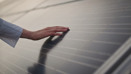 A woman holds his hand above the surface of the sun panels. Close up of a young engineer hand is checking the operation of sun and cleanliness of photovoltaic solar panels on a sunset.