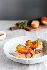 Summer Breakfast - toast (sandwich, bruschetta) with grilled peaches, cream cheese (ricotta, mascarpone), thyme and honey on beige linen tablecloth. Selective focus