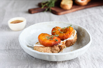 Summer Breakfast - toast (sandwich, bruschetta) with grilled peaches, cream cheese (ricotta, mascarpone), thyme and honey on beige linen tablecloth. Selective focus